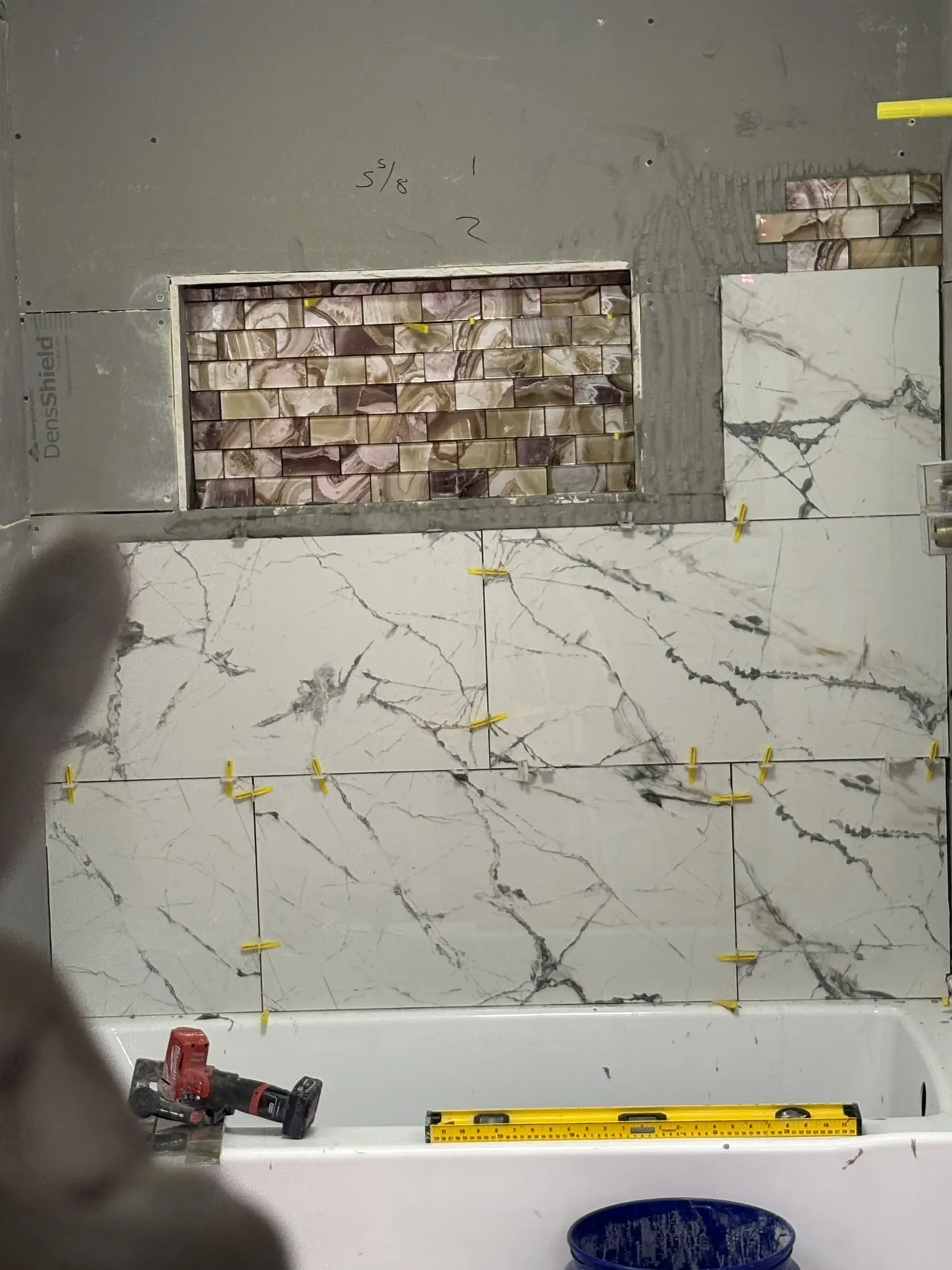 Veined tile and mosaic being installed around the bathtub niche.